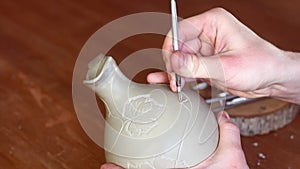 Potter carving ornament on jug. Master working in Pottery studio with equipment Wooden Modeling Tools set