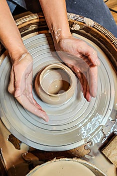 Potter clay pottery pot craft wheel hands. Potter's hands while working on the wheel, top view with dark background.