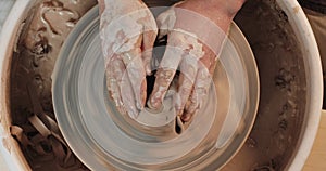 Potter hands breaks clay plate on twisted potter`s wheel. Pottery training, artwork concept. Top view. White clay