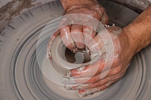 Potter with his hands beginning the transformation of piece of white clay into the pot on the wheel circle in studio. Concept of