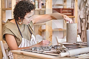 Potter imprinting designs on a clay cylinder.