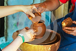 Potter makes on the pottery wheel clay pot and conducts a master class. Hands of the master and child close-up during work.