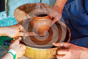 Potter makes on the pottery wheel clay pot and conducts a master class. Hands of the master and child close-up during work.