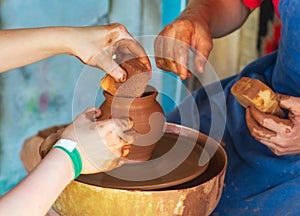 Potter makes on pottery wheel clay pot and conducts a master class. Hands of the master and child close-up during work. Ancient