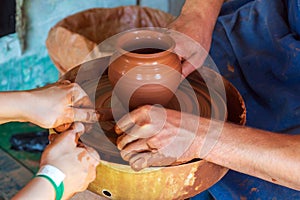 Potter makes on the pottery wheel clay pot and conducts master class. Hands of the master and child close up during work. Ancient