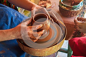 Potter makes on pottery wheel clay pot and conducts master class. Hands of master and child close up during work. Ancient national