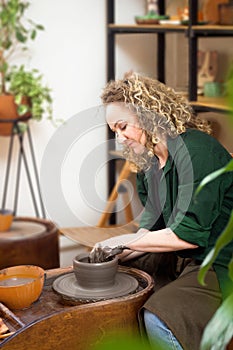 Potter molds pot. Blonde Curly Woman on pottery workshop. Clay bowl spinning on pottery wheel. Ceramic class studio