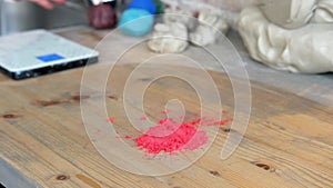 The potter pours red powdered dye on a wooden table, then washes his hands