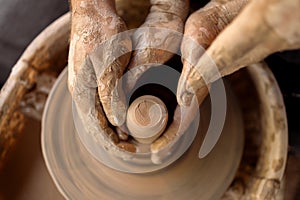 Potter's hands guiding female hands to help her to work with clay on the pottery wheel