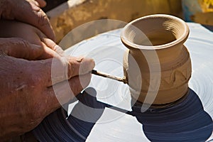 Potter`s hands make an ornament on clay bowl on a pottery wheel