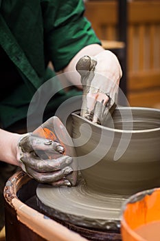 Potter& x27;s hands molds pot with tool close up. Woman works in pottery workshop. Clay bowl spinning on pottery wheel