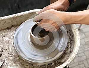 Potter`s hands with the product on a potter`s wheel.the dirty hands making pottery in clay on wheel