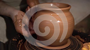 Potter`s hands shaping up the terracotta clay pot on wheal.