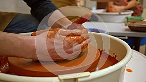 On a potter`s wheel, a bowl of orange clay, which is formed by the hands of a potter, rotates