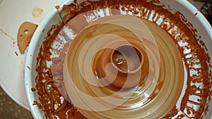 A potter`s wheel with an orange clay jug is rotating top view