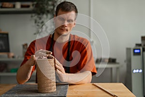 Potter sculpts a patterned cylinder from clay.