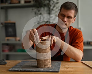 Potter sculpts a patterned cylinder from clay. photo