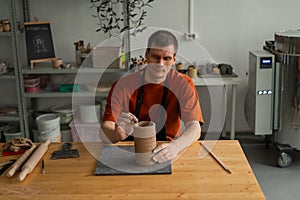 Potter sculpts a patterned cylinder from clay.