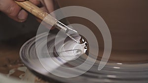 Potter shapes clay product with pottery tools on potter`s wheel. Potter`s hands