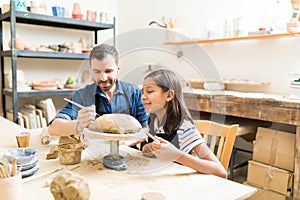 Potter Showing Girl To Make Design On Clay In Pottery Studio