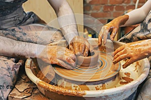 potter teaches the child. A craftsman sits on a bench with a potter& x27;s wheel and makes a clay pot. National craft