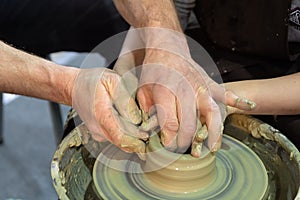 A potter teaches a child to work with clay on a pottery wheel