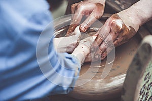 Potter teaching a girl to make clay pot on potter`s wheel.