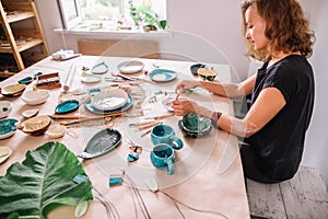 Potter woman paints ceramic cup. Woman working In her pottery studio