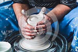 Potter at work on a pottery wheel with white clay. Hands of the master.