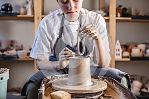 Potter working on a Potter`s wheel making a vase. Young woman forming the clay with hands creating jug in a workshop