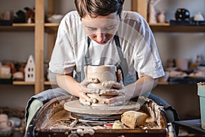 Potter working on a Potter`s wheel making a vase. Young woman forming the clay with hands creating jug in a workshop