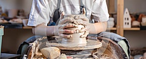 Potter working on a Potter`s wheel making a vase. Young woman forming the clay with hands creating jug in a workshop