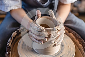 Potter working on a Potter`s wheel making a vase. Woman forming the clay with hands creating jug in a workshop. Close up