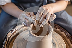 Potter working on a Potter`s wheel making a vase. Woman forming the clay with hands creating jug in a workshop. Close up