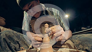 A potter works with special equipment, close up. A man creates a clay vase, shaping it on a special wheel.