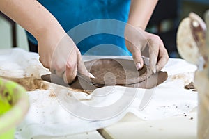 Pottering Concepts. Closeup of Hands of Female Worker Cutting A plate of Wet Clay on Table Before Moulding