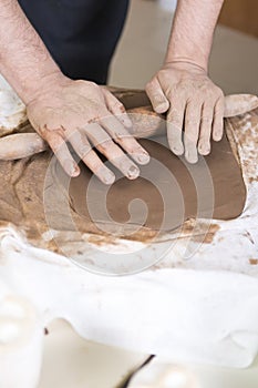 Pottering Ideas and Concepts. Closeup of Hands of Male Worker Rolling a Piece of Wet Clay on Table Before Moulding