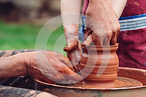 Potters and child hands. Pottery workshop outside. Master teaching kid to creating on the pottery wheel