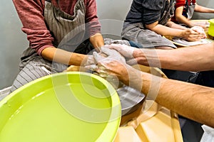 Potters hand correcting womans ones during shaping clay blank on a potters wheel. Pottery lesson, hobby