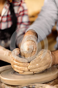 Potters hands guiding a woman hands to help her to work with the ceramic wheel