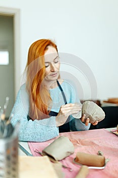 Pottery studio, artisan business,red hair female potter holding ceramic bowl ready for firing in a kiln