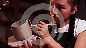 Pottery in the studio - asian woman holding a cup on the plate and smearing parts of clay on the joint on the handle and