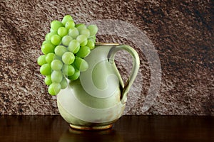 Pottery Wine Jug with Grapes on a Wooden Table with a Mottled Background