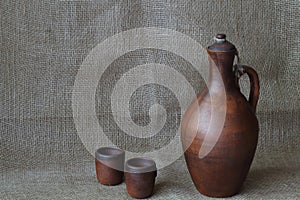 Pottery, wine set: clay jar and cups on a rough jute homespun cloth. Concept â€” kitchen utensils, rustic style, pottery. Minimal