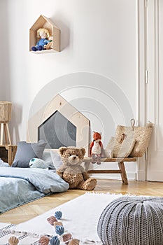 Pouf, carpet, toys and bed with blue bedding in stylish little boy`s bedroom, real photo