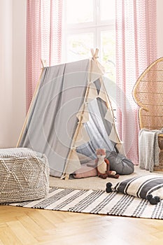 Pouf on patterned rug near tent with fox toy in girl`s room with pink drapes and pillows. Real photo