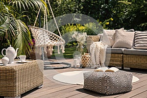Pouf on wooden terrace with rattan sofa and table in the garden with hanging chair. Real photo photo