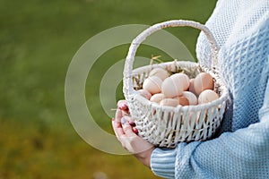 Poultry eggs lie in wicker basket in hands of woman.