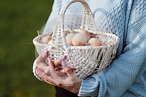 Poultry eggs lie in wicker basket in hands of woman.