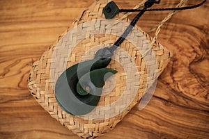 Pounamu fish hook necklace on grainy wooden background. Aotearoa, New Zealand, Maori. Side angle view.